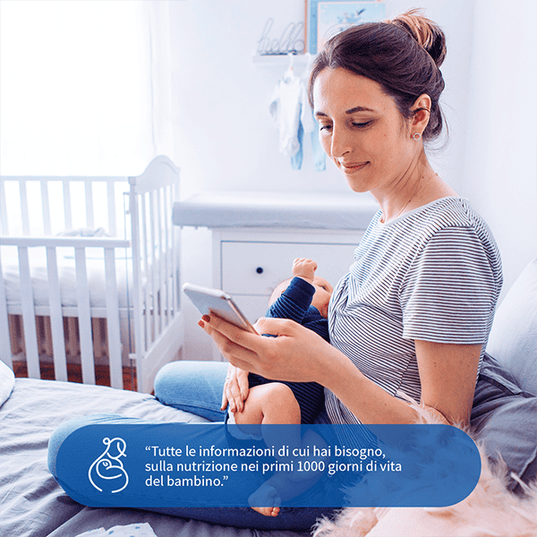 Mamma che utilizza il telefono con bambino in braccio in stanza luminosa.