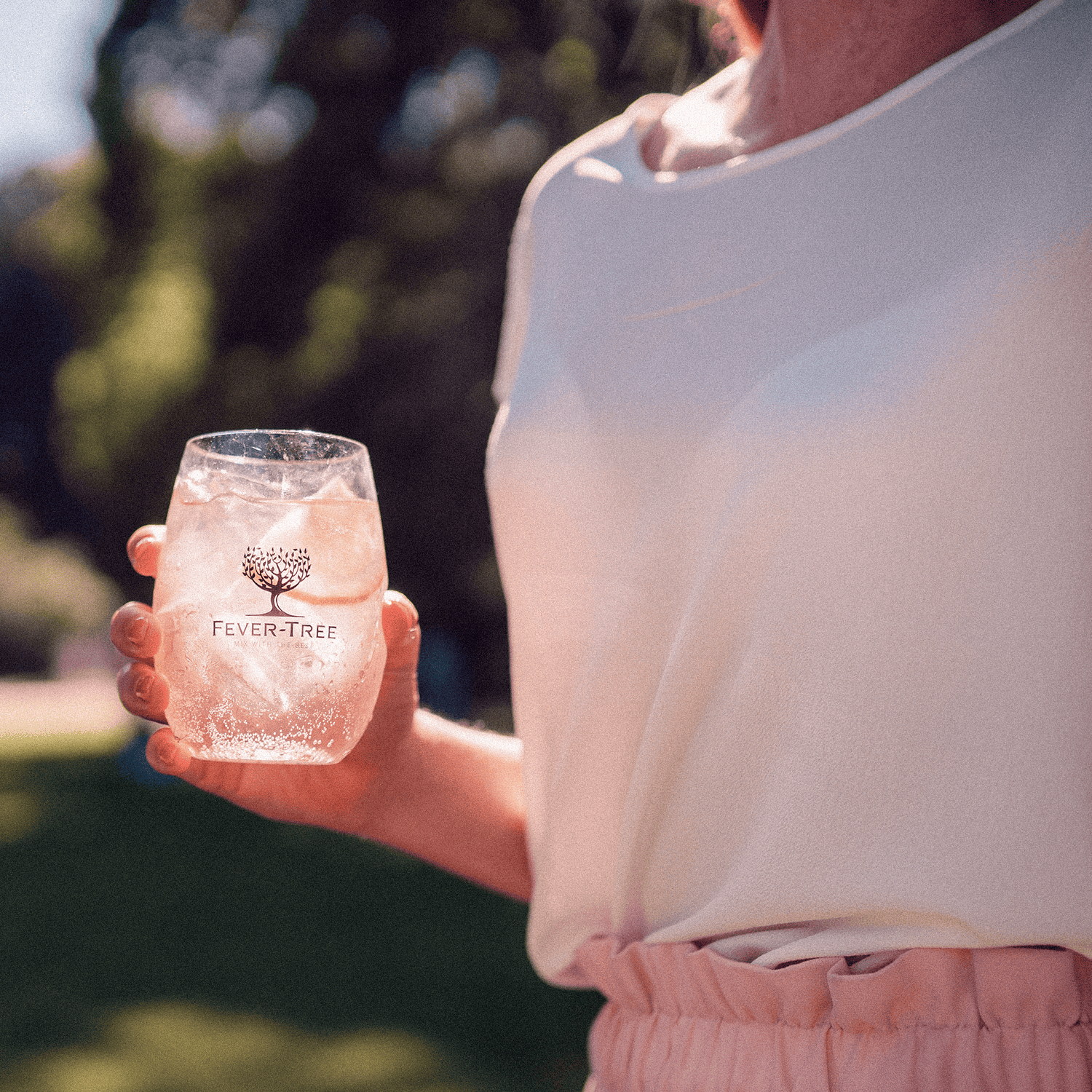 Persona che tiene un bicchiere di Fever Tree all'aperto in un parco.